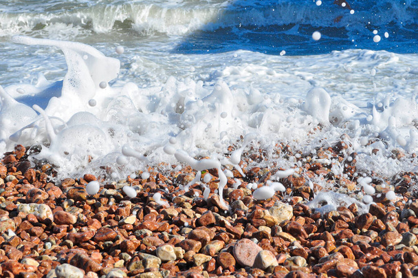 Piedras marinas, guijarros, espuma marina, guijarros en la orilla del mar, salpicaduras de agua sobre piedras, fondo con piedras mojadas, guijarros en la playa, olas marinas sobre guijarros - Foto, Imagen