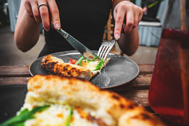 manos de mujer con cuchillo y tenedor corte pizza en la mesa en la cafetería al aire libre - Foto, Imagen
