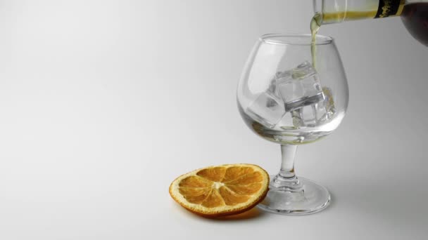 ένα ποτήρι ουίσκι με πάγο και μια φέτα πορτοκάλι σε λευκό φόντο - Πλάνα, βίντεο