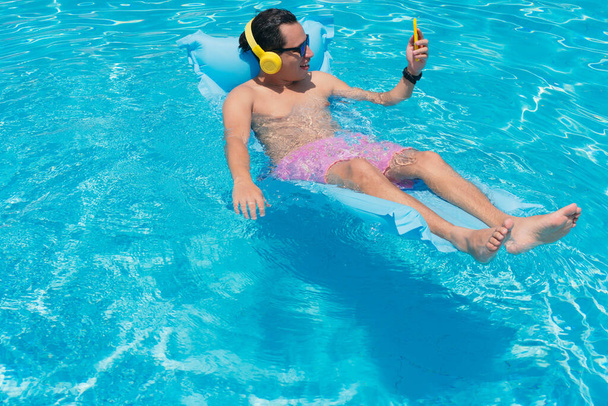 Молодой человек в бассейне пользуется мобильным телефоном. - Фото, изображение