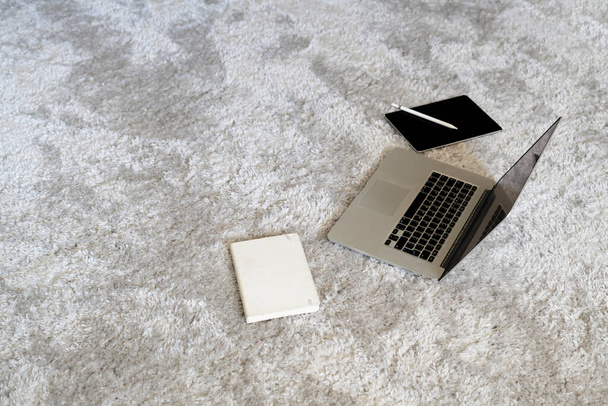 un ordinateur portable et d'autres dispositifs sur le sol sur le tapis mou dans le salon à la maison, l'isolement pendant la pandémie de coronavirus - Photo, image