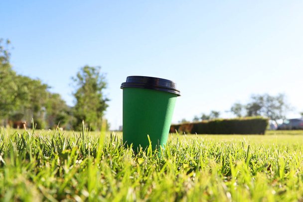 Green paper coffee cup on the grass in a sunny day. Summer outdoor leisure. Photo with selective focus - Foto, Imagem