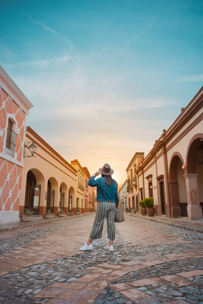 Tourist woman standing in the middle of the street of a magical town, town of La Pena del Bernal in Queretaro, Mexico, with sunset in front, summer day - Fotoğraf, Görsel