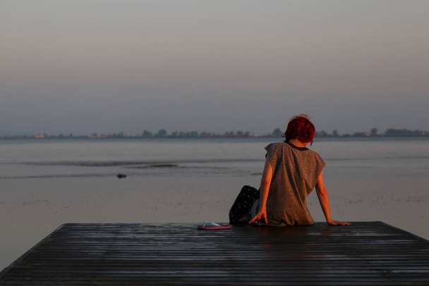 Γυναίκα κάθεται σε ξύλινη αποβάθρα με θέα στη θάλασσα στο δέλτα του Έβρου - Φωτογραφία, εικόνα