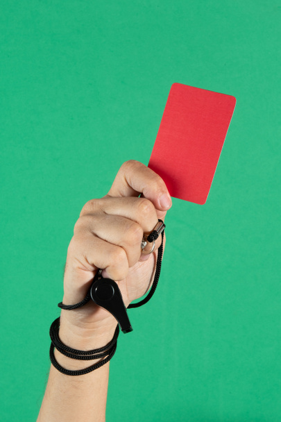 mano dell'arbitro in possesso di un cartellino rosso e fischio su sfondo verde. - Foto, immagini