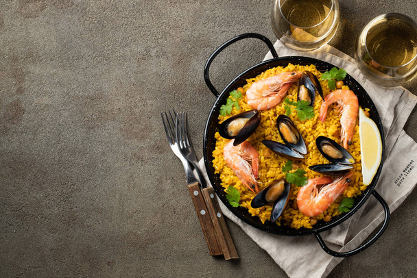 Traditionele Spaanse zeevruchten paella in pan met kikkererwten, garnalen, mosselen, inktvis op bruine betonnen achtergrond. Bovenaanzicht met kopieerruimte - Foto, afbeelding