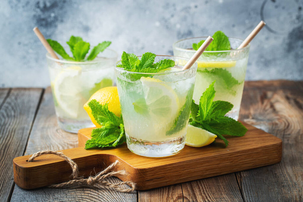 Dvě sklenice s limonádou nebo mojito koktejl s citrónem a mátou, studený osvěžující nápoj nebo nápoj s ledem na rustikálně modrém pozadí - Fotografie, Obrázek