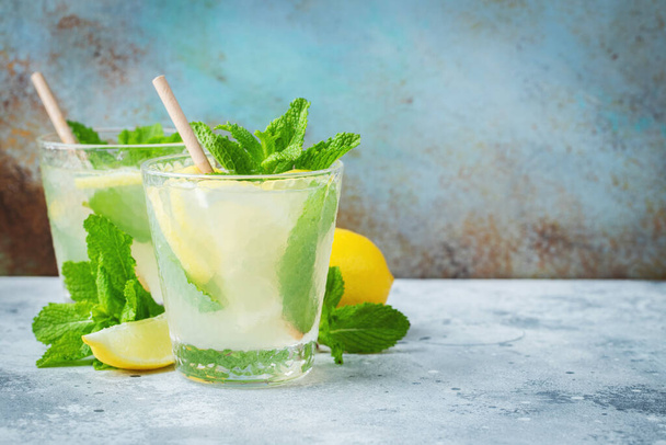 Twee glazen met limonade of mojito cocktail met citroen en munt, koud verfrissend drankje of drankje met ijs op rustieke blauwe achtergrond. Kopieerruimte - Foto, afbeelding