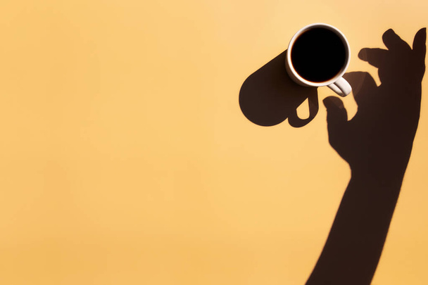 Chávena branca e prato de pires de café expresso preto de vista superior com sombra de sol e mão segurando ou tocando a xícara em fundo de terracota bege amarelo. Foto de alta qualidade - Foto, Imagem