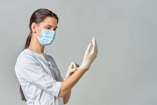 лікар в білому пальто і медична маска кладе стерильні білі латексні рукавички на руки для процедури, копіювати простір
 - Фото, зображення
