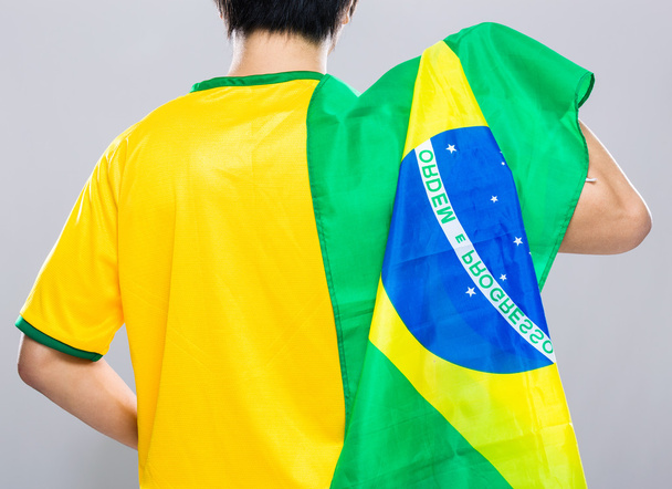 Бразильский футбольный болельщик держит флаг Бразилии
 - Фото, изображение