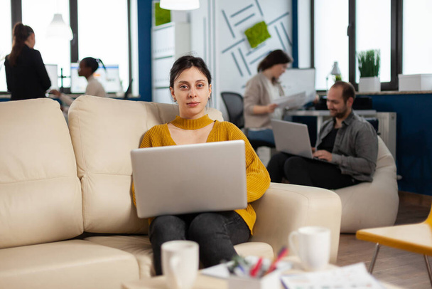 Молода жінка-підприємець, сидячи на дивані посеред офісу стартапу бізнесу
 - Фото, зображення