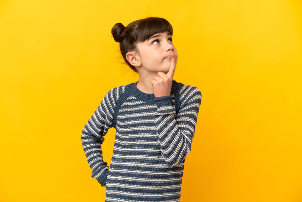 Kleines kaukasisches Mädchen isoliert auf gelbem Hintergrund mit Zweifeln beim Nachschauen - Foto, Bild
