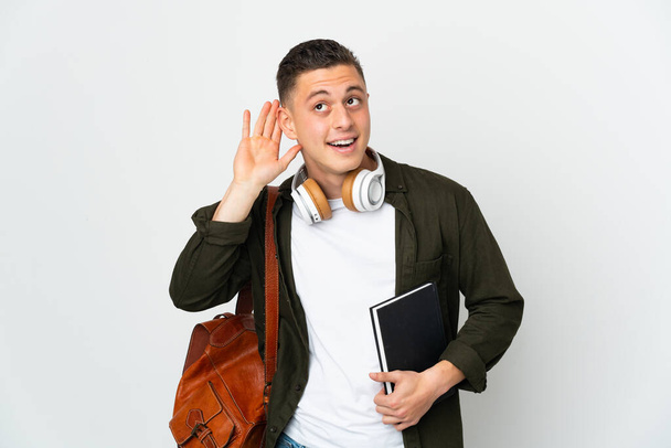 Νεαρός καυκάσιος φοιτητής απομονωμένος σε λευκό φόντο ακούγοντας κάτι βάζοντας το χέρι στο αυτί - Φωτογραφία, εικόνα