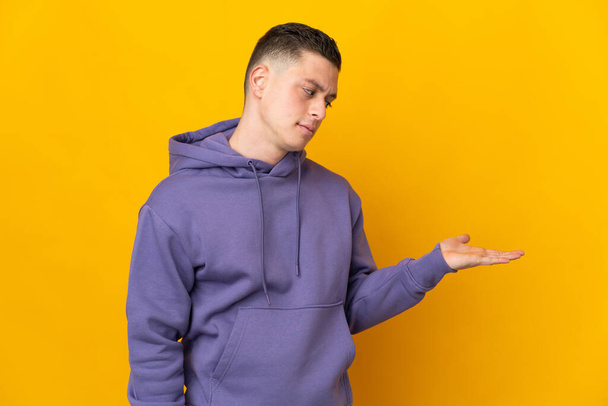 Young caucasian man isolated on yellow background holding copyspace with doubts - Foto, Bild