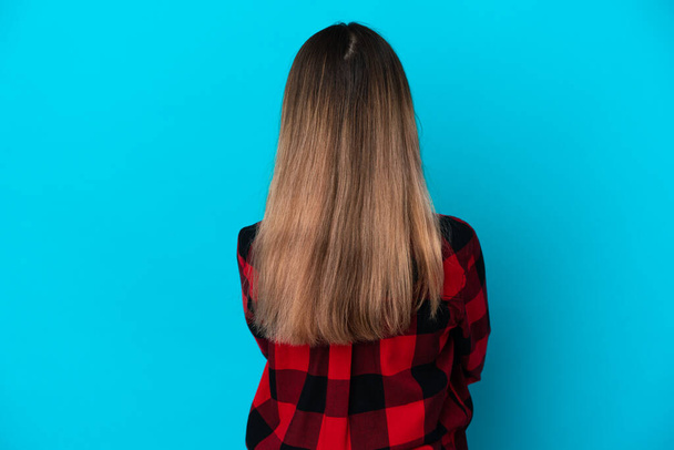 Giovane donna caucasica isolata su sfondo blu in posizione posteriore - Foto, immagini