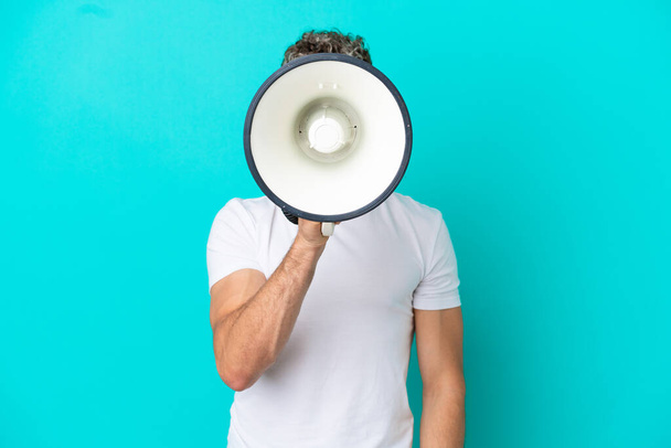 Young handsome caucasian man isolated on blue background shouting through a megaphone to announce something - Foto, afbeelding