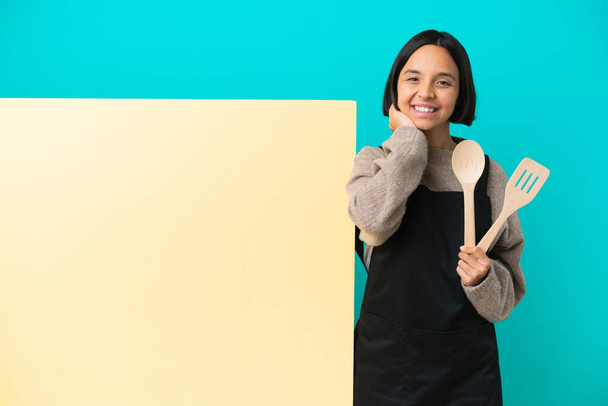 Young mixed race cook woman with a big placard isolated on blue background laughing - Photo, Image