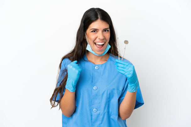 Dentist woman holding tools over isolated white background celebrating a victory in winner position - Fotó, kép