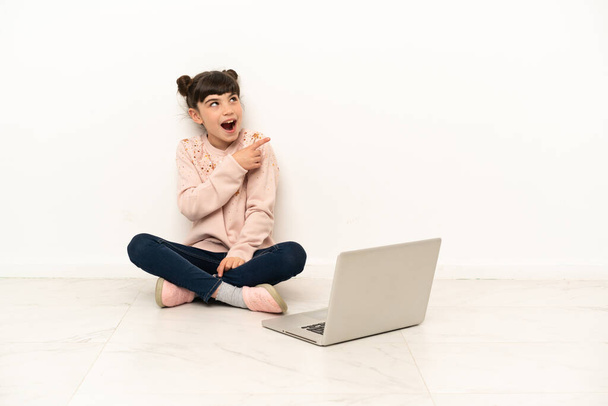 Egy laptoppal a padlón ülő kislány, aki rá akar jönni a megoldásra, miközben felemeli az ujját. - Fotó, kép