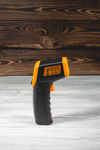 Pirómetro amarillo-negro sobre fondo de madera. Dispositivo para la medición de temperatura sin contacto. Estudio foto. - Foto, imagen