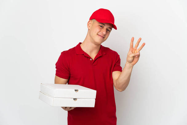 Pizzabote in Arbeitsuniform nimmt Pizzakartons isoliert auf weißem Hintergrund glücklich entgegen und zählt mit den Fingern drei - Foto, Bild