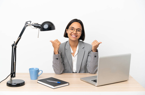 Jonge zaken gemengde ras vrouw werken op kantoor met duimen omhoog gebaar en glimlach - Foto, afbeelding