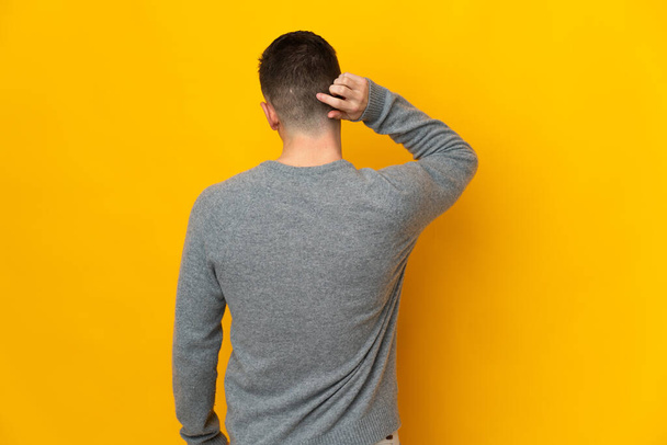 Young caucasian man isolated on yellow background in back position and thinking - Photo, image