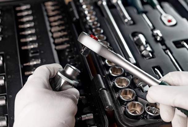 Hands of repairman in gloves close up with metal steel socket ratchet handle over toolbox, POV - Zdjęcie, obraz