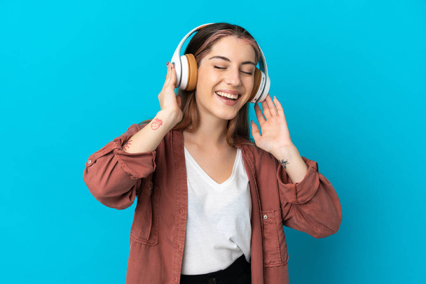 Young caucasian woman isolated on blue background listening music and singing - Foto, Imagem