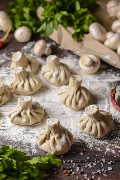 Georgian dumpling or Khinkali. Georgian homemade khinkali on wooden background. Side view, selective focus. With fresh greenery, spices and raw mushrooms. - Photo, Image