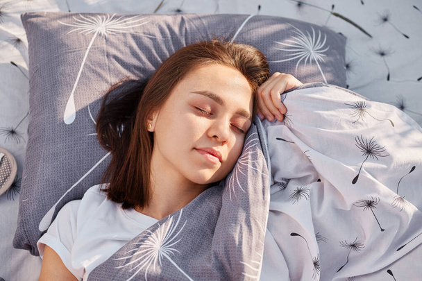 Young adult dark haired female with closed eyes lying on soft pillow under blanket and resting, relaxing outdoor, spending time on nature, enjoying fresh air. - Fotó, kép