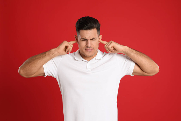 Man covering ears with fingers on red background - Photo, image