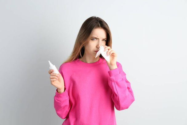 Sick young woman with nasal spray and tissue on white background - Foto, immagini