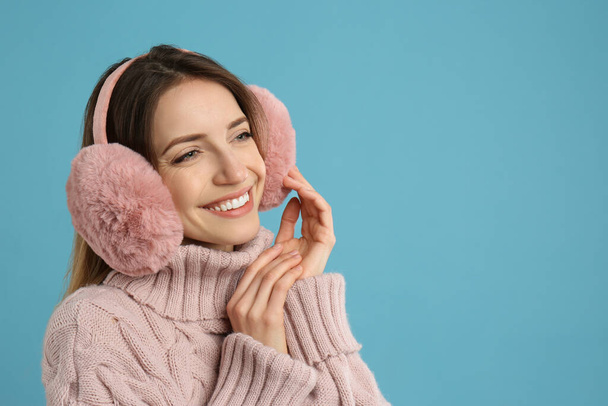 Happy woman wearing warm earmuffs on light blue background, space for text - Photo, image