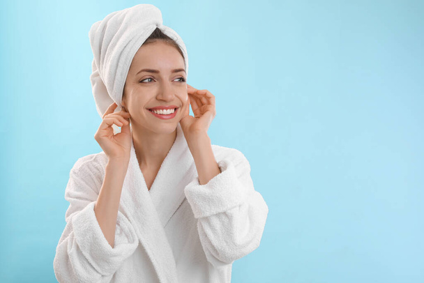 Beautiful young woman with hair wrapped in towel after washing on light blue background. Space for text - Foto, immagini