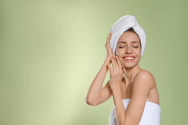 Beautiful young woman with hair wrapped in towel after washing on light green background. Space for text - Foto, immagini