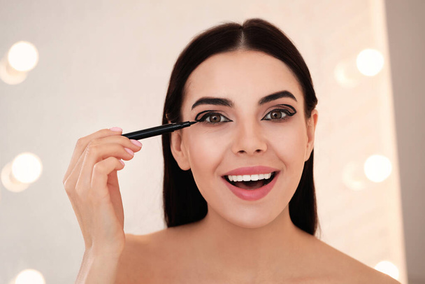 Beautiful young woman applying black eyeliner indoors - Foto, Imagem