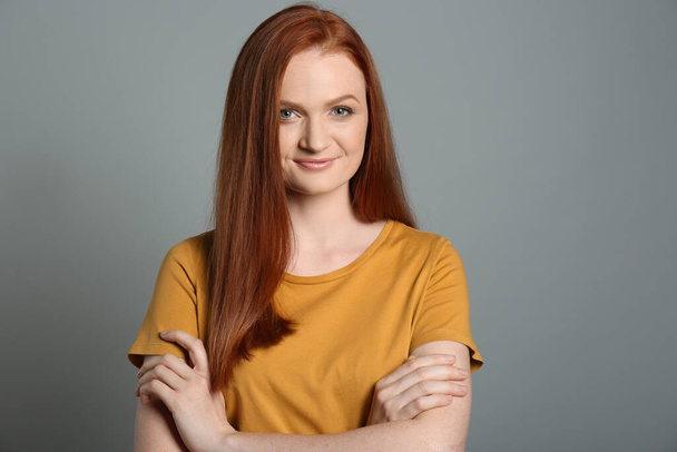 Candid portrait of happy young woman with charming smile and gorgeous red hair on grey background - Fotó, kép