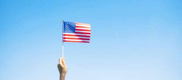 ręka trzymająca flagę Stanów Zjednoczonych Ameryki na tle błękitnego nieba. USA święto weteranów, Memoriał, Niepodległość (4 lipca) i koncepcja Dnia Pracy - Zdjęcie, obraz