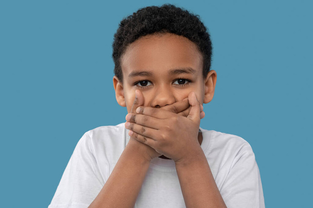 Веселый мальчик закрывает рот ладонями - Фото, изображение