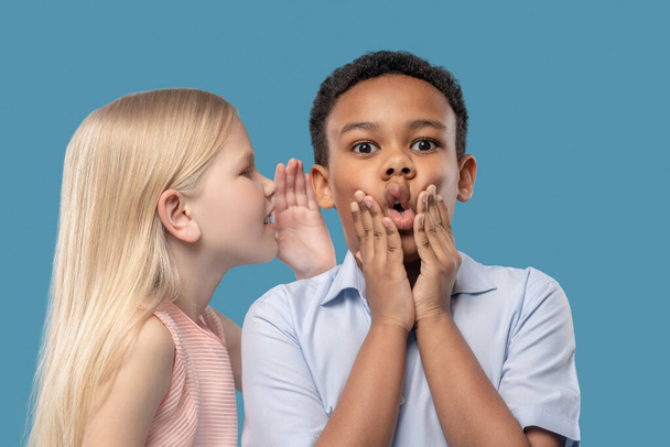 Девушка рассказывает секрет в ушах шокированного мальчика - Фото, изображение