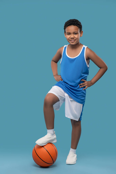Joyful boy in sportswear holding ball with foot - Foto, afbeelding