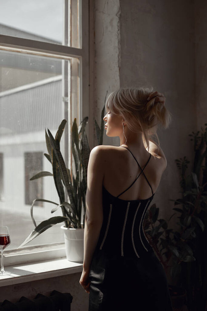 Retro portrait sexy blonde woman in black dress, vintage interior woman posing at window. Sensual romantic look, girl relaxes at home - Фото, изображение