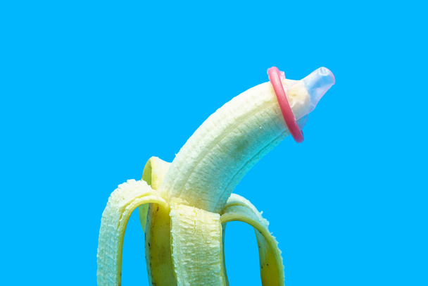 El condón lleva un plátano sobre un fondo azul. Concepto de prevención sexual segura de enfermedades de transmisión sexual y anticonceptivos. - Foto, Imagen