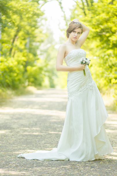 Portrait of a beautiful young bride in nature. Young woman holding a small bouquet of white roses in her hands - Photo, image