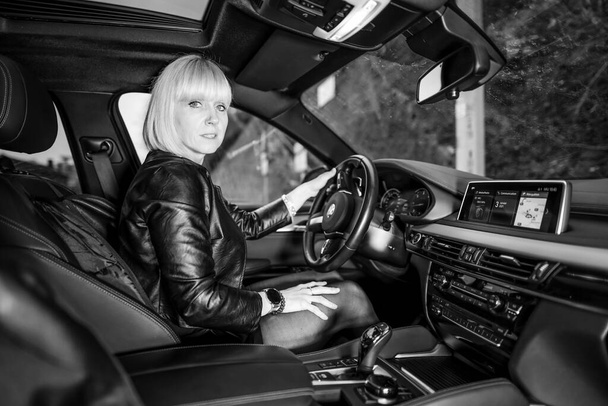 black and white portrait of beautiful blonde woman in car at parking lot - Фото, изображение