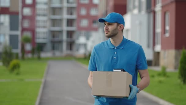 Un repartidor lleva un paquete a los clientes en una zona residencial. Entrega de comestibles y compras online - Metraje, vídeo