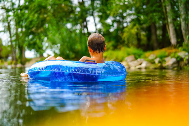 Boy relaxing lonely in a blue buoy in a wild river - Foto, afbeelding