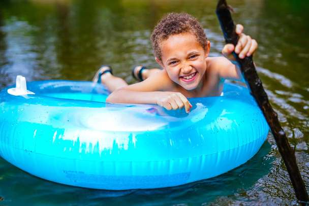 Niño jugando en boya inflable azul en río salvaje - Foto, Imagen